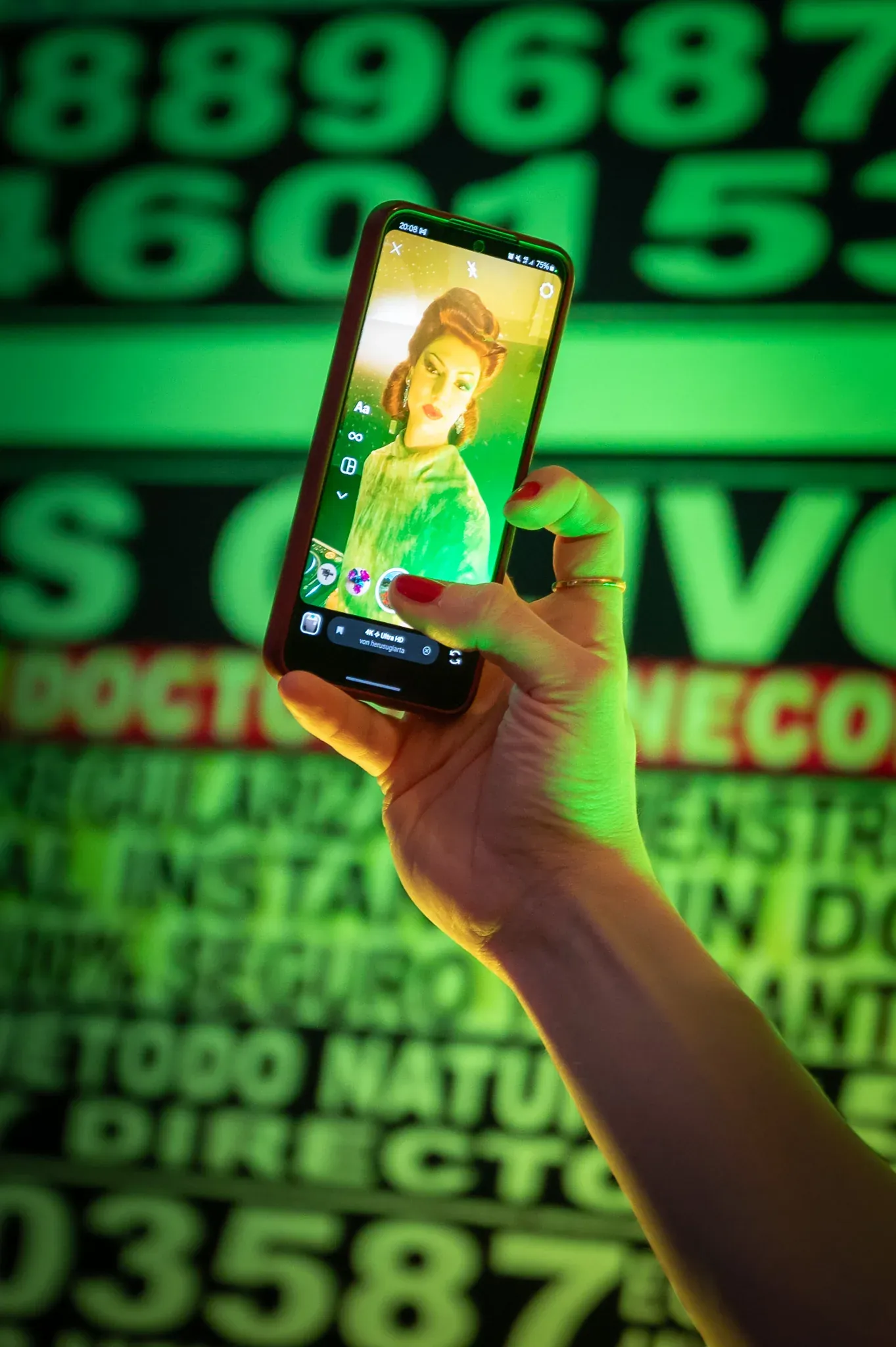 Hand mit Smartphone vor einer grün leuchtenden Typografie-Wand.