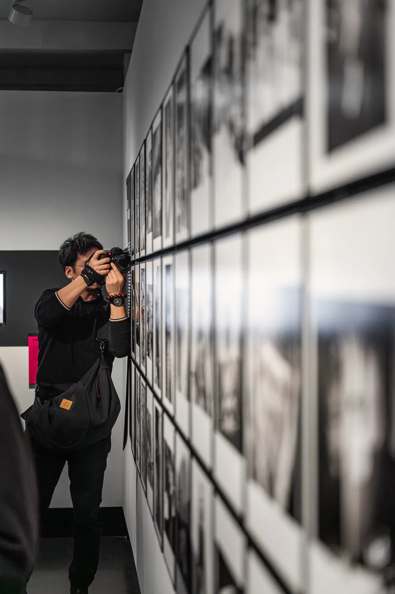 Person fotografiert eine lange Wand mit gerahmten Schwarzweißbildern.