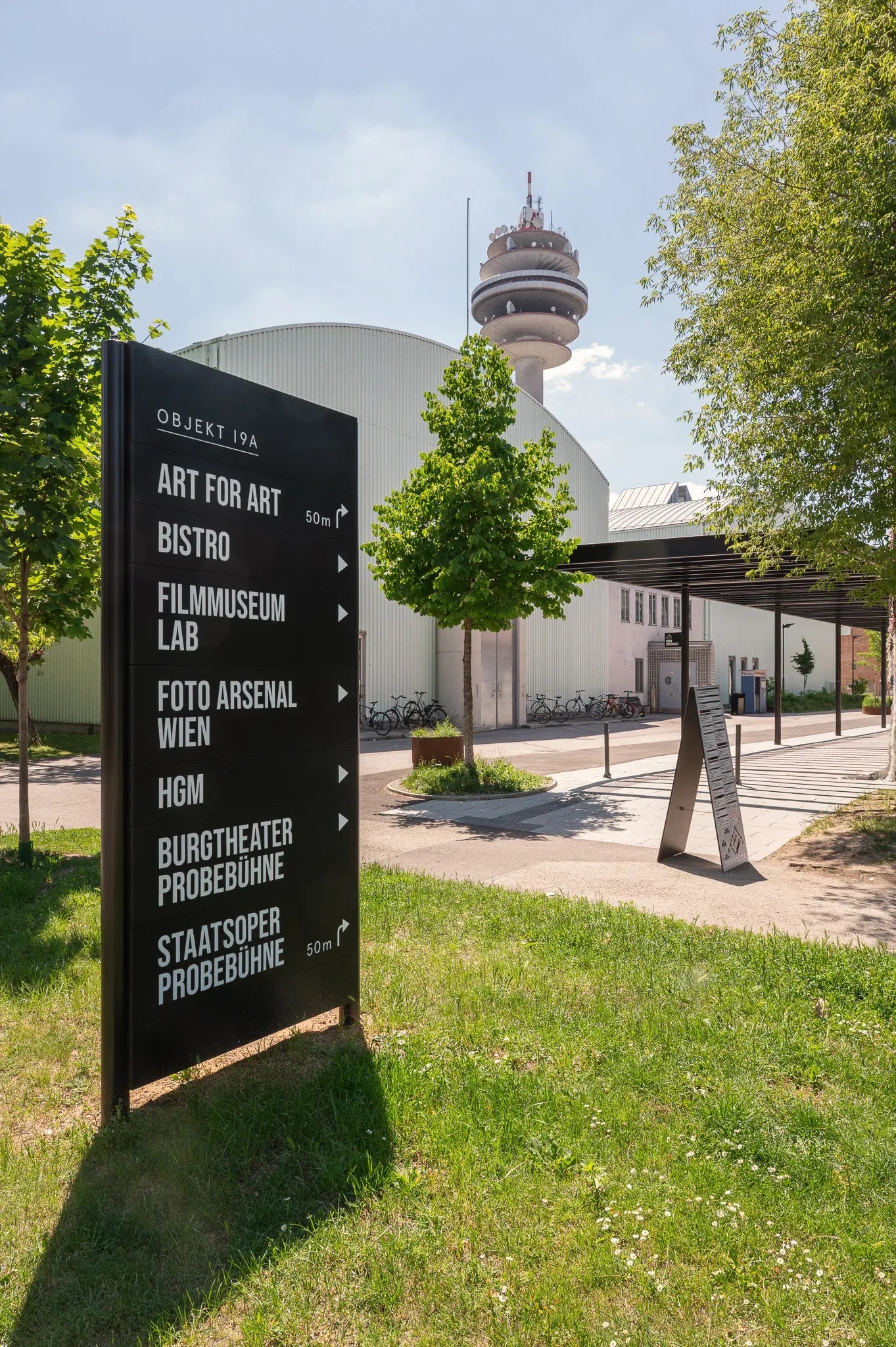 Beschilderung des Foto Arsenal Wien im Grünen, Turm im Hintergrund.