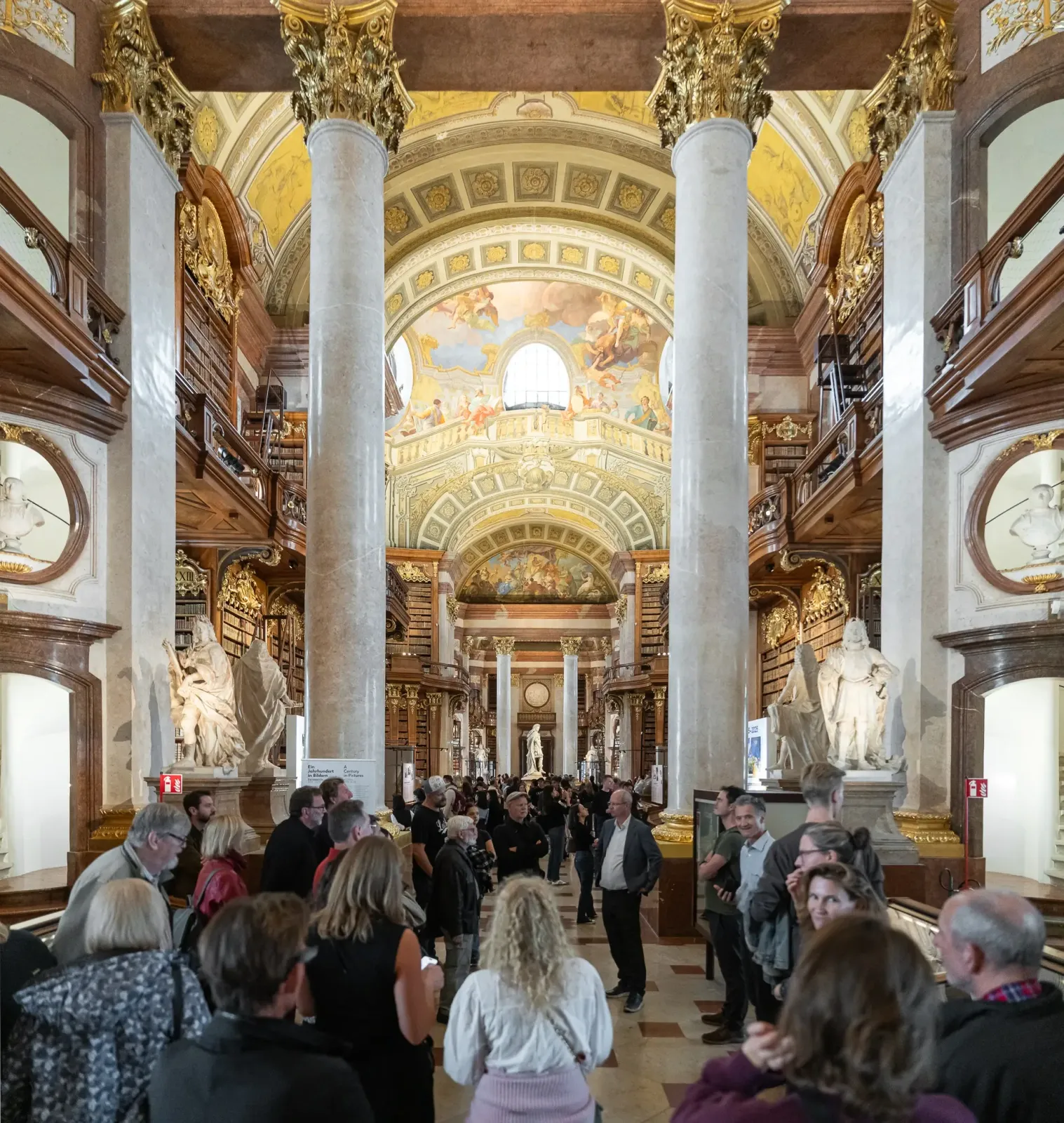 Prunksaal der Nationalbibliothek: Gäste zwischen Marmorsäulen unter dem Deckenfresko.
