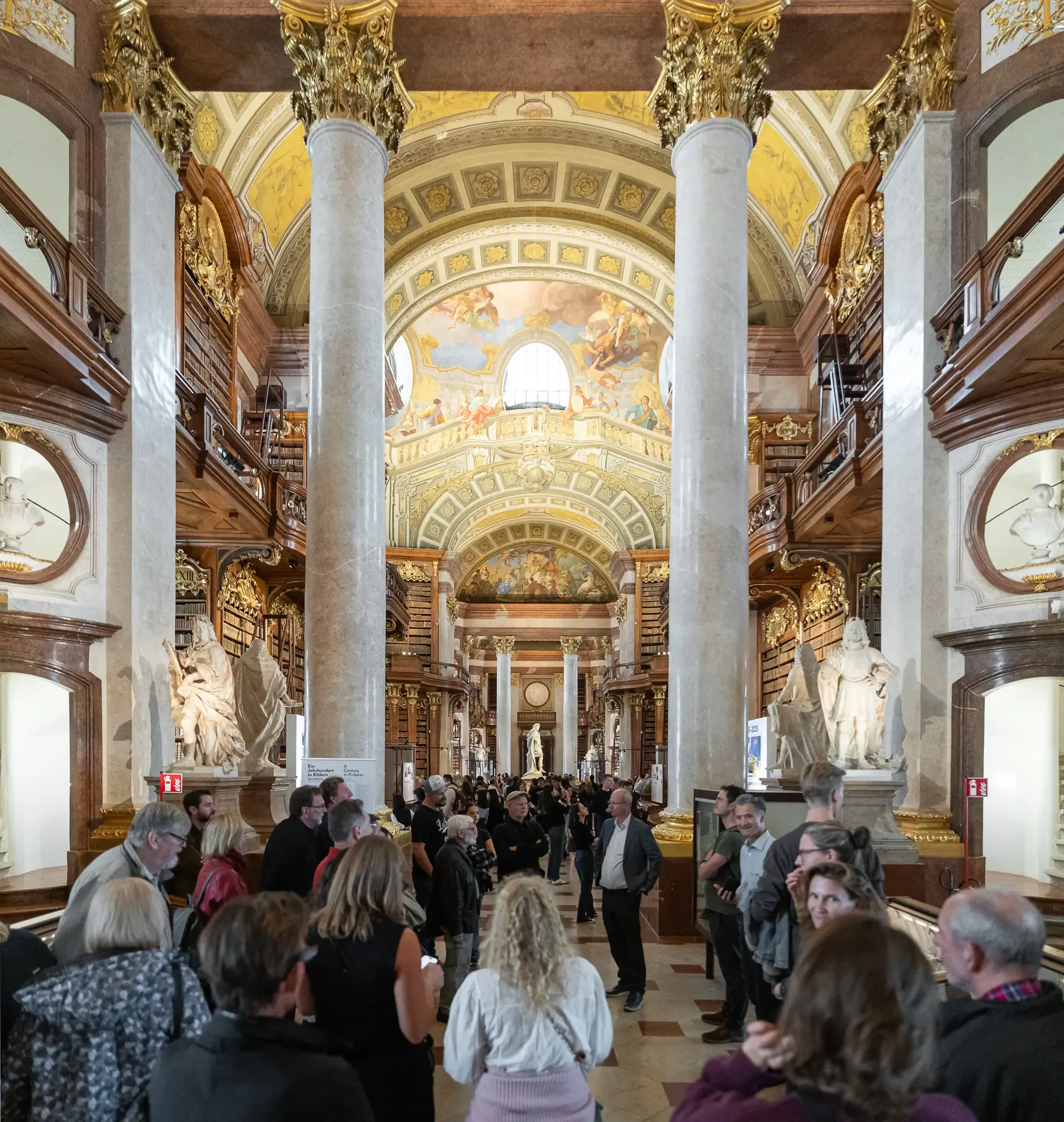 Prunksaal der Nationalbibliothek: Gäste zwischen Marmorsäulen unter dem Deckenfresko.