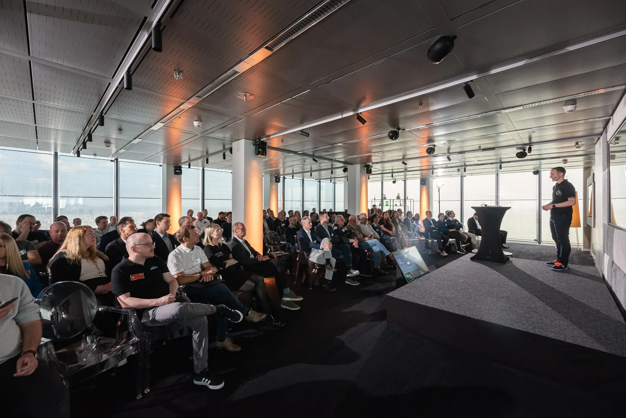 Konferenzraum mit Publikum und Fensterfront über der Stadt.